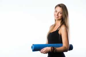 Studio shot of young beautiful teenage girl holding yoga mat and posing ready for gym